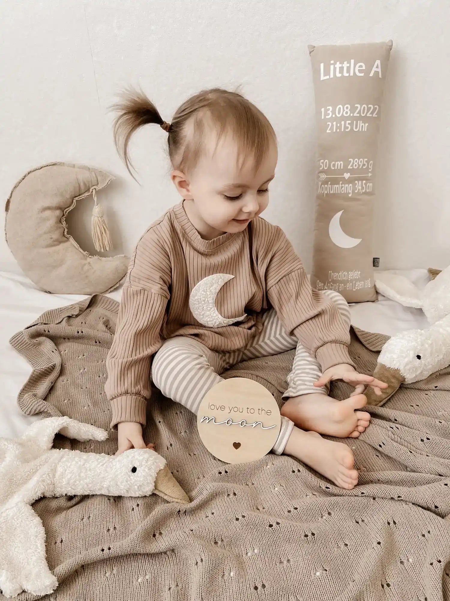 Ein bezauberndes Baby trägt ein geripptes langärmeliges Oberteil mit einem Mond-Grafik und gestreiften Leggings.